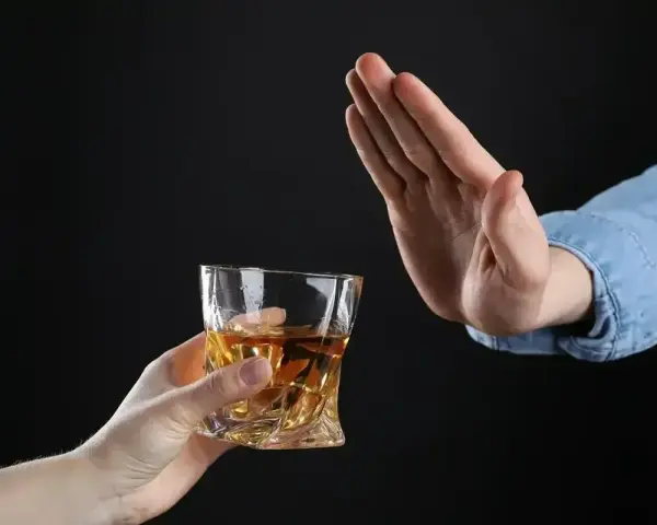 Dłoń odrzuca szklankę z bursztynowym płynem. Pytanie: czy po znieczuleniu u dentysty można pić alkohol?