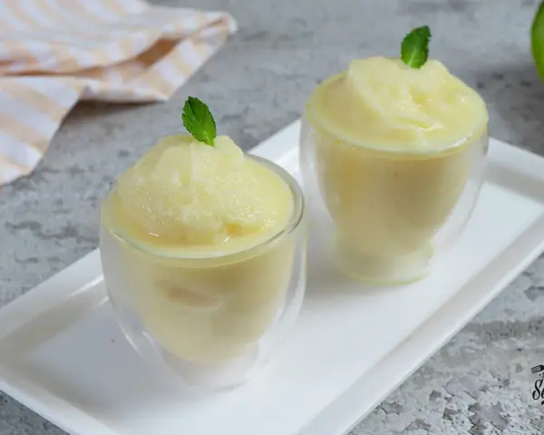 Dos copas de refrescante sorbete de melón, decoradas con hojas de menta, listas para disfrutar en un día caluroso.