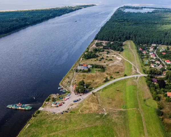 Widok na Wisłę i jej ujście. Prom przewozi samochody, a w oddali widać las i zabudowania.