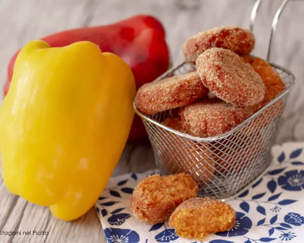 Polpette di peperoni dorate e croccanti, servite in un cestino, accanto a peperoni freschi rossi e gialli.