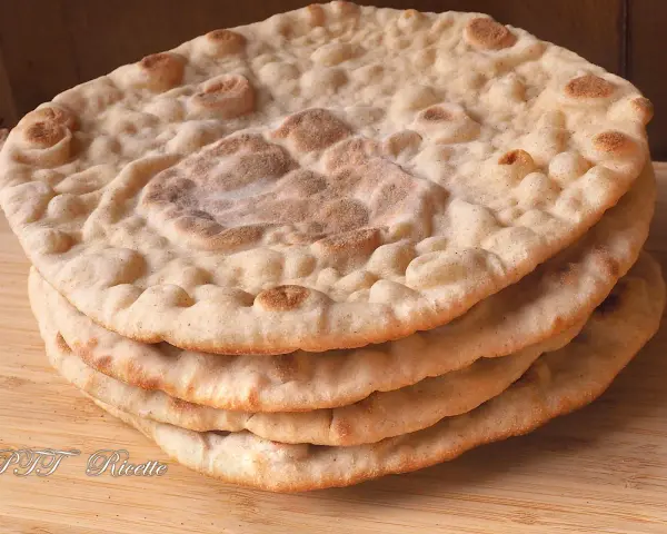 Una pila di pane naan senza lievito, dorato e soffice, su un tagliere di legno.