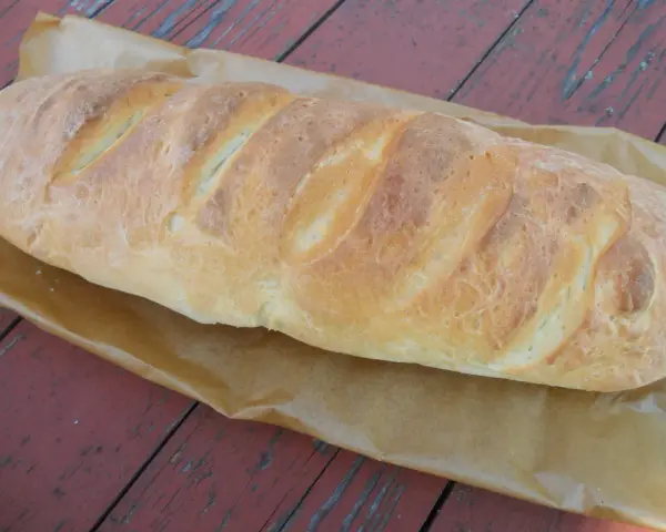Złocista bułka paryska, świeżo upieczona, leży na papierze do pieczenia na drewnianym stole.