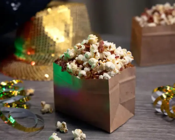 Festliga popcornboxar med bacon, redo för nyårsfirande. Glitterband och en paljetthatt i bakgrunden skapar en festlig stämning.