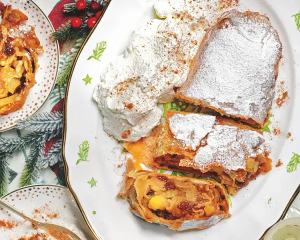 Delizioso strudel di mele con pasta sfoglia, cosparso di zucchero a velo e servito con panna montata e cannella.