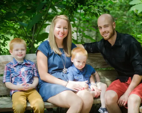 Rodzina na ławce w parku. Dwóch rudowłosych chłopców, mama i tata uśmiechają się. Młodszy syn, jakby w uporczywe naśladowanie innych dzieci, siedzi na kolanach mamy.