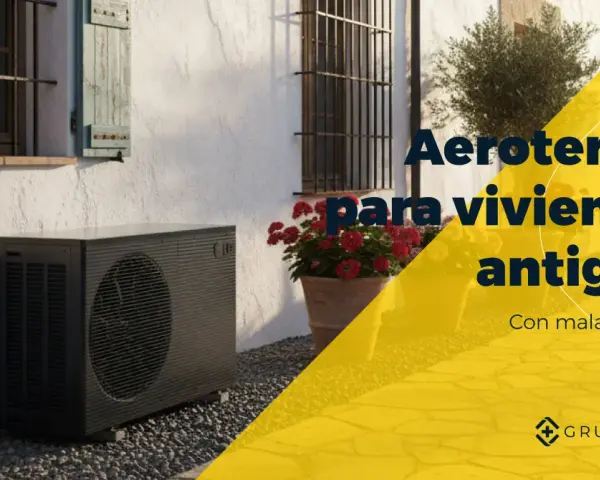 Unidad exterior de bomba de calor aire-agua junto a una casa antigua con flores. Aerotermia para viviendas antiguas.