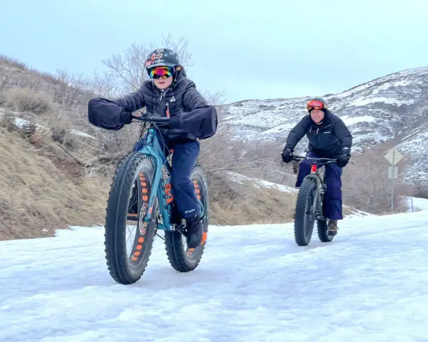 Two people ride fat tire bikes on a snowy path, demonstrating what are fat tire bikes for: tackling challenging winter terrain with their wide tires.