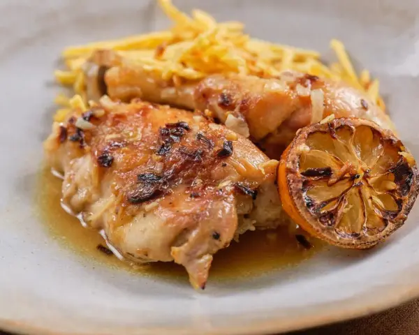 Delicioso pollo al limón con papas fritas crujientes y una rodaja de limón caramelizada.
