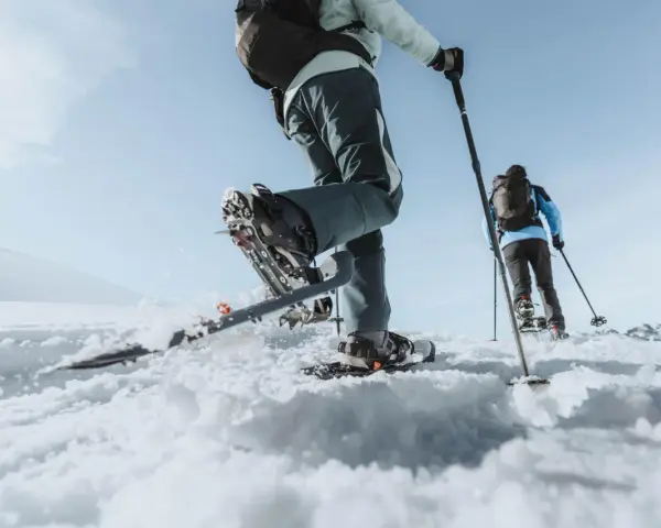 Deux personnes font une randonnée hivernale en raquettes sur un paysage enneigé sous un ciel bleu clair.