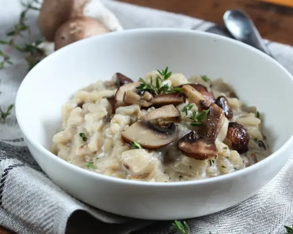 Kremowe risotto z pieczarkami i świeżym tymiankiem w białej misce.