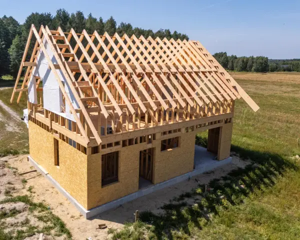 Budowa domu szkieletowego z widoczną drewnianą konstrukcją dachu i ścianami z płyt OSB.