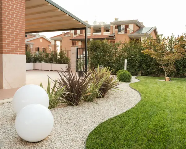 Giardino moderno con ghiaia bianca, sfere luminose e piante decorative. Belle idee giardino ingresso casa per un'accoglienza elegante.