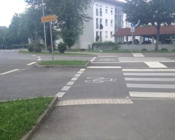 Ein Zebrastreifen mit Fahrradsymbolen auf dem Asphalt. Ein Schild weist in alle Richtungen.