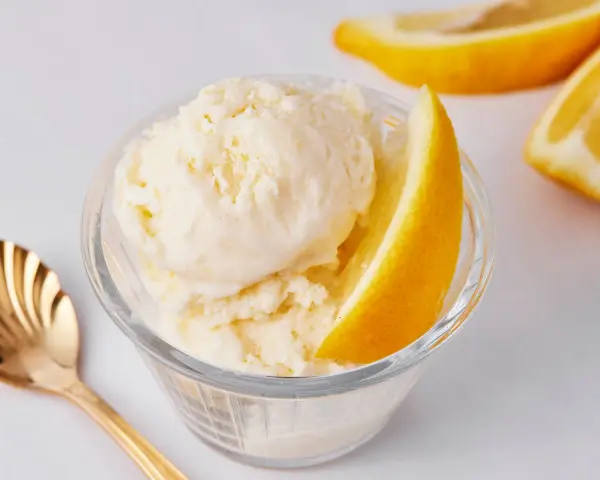 Erfrischendes Zitroneneis selber machen: Cremiges Eis im Glas mit Zitronenspalte und goldener Löffel.