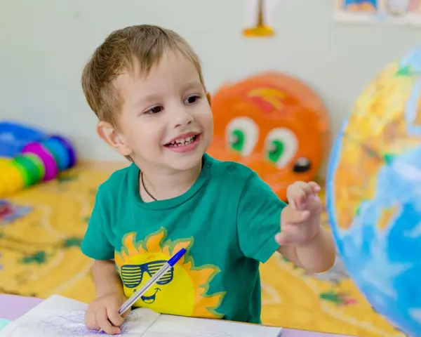 Uśmiechnięte polskie dziecko w hiszpańskiej szkole bawi się globusem i rysuje w zeszycie.