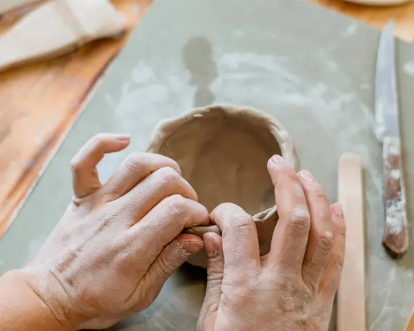 Mani che modellano argilla per creare una ciotola. Utensili da ceramica e un coltello sono visibili. Un ottimo punto di partenza per chi cerca dove trovare l'argilla.