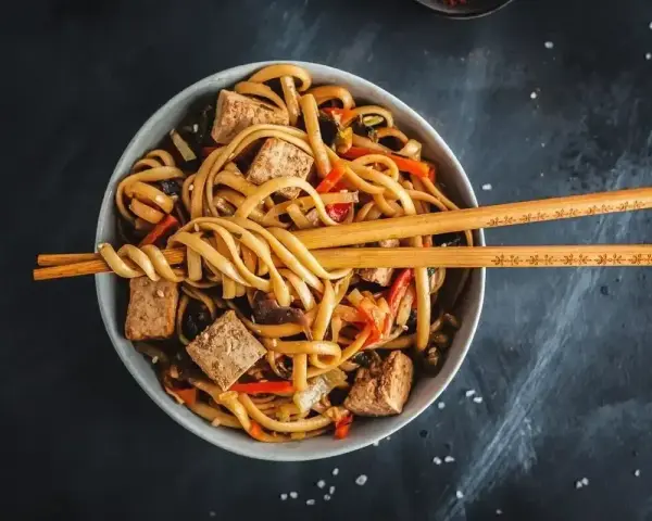 Miseczka z makaronem udon, tofu i warzywami, gotowa do podania. Idealny przepis na pad udon.
