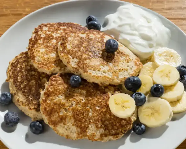En tallrik med bananpannkakor, blåbär, bananskivor och en klick yoghurt. Ett enkelt bananpannkaka recept för en god frukost.