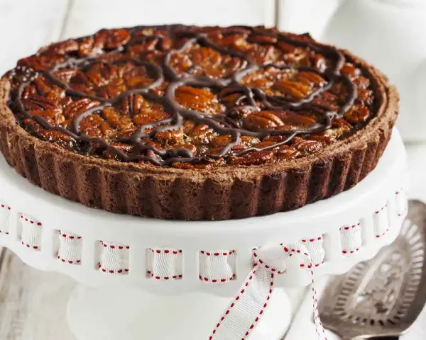 Deliziosa crostata al cioccolato con noci pecan caramellate e un elegante motivo di cioccolato fuso. Perfetta per ogni occasione.
