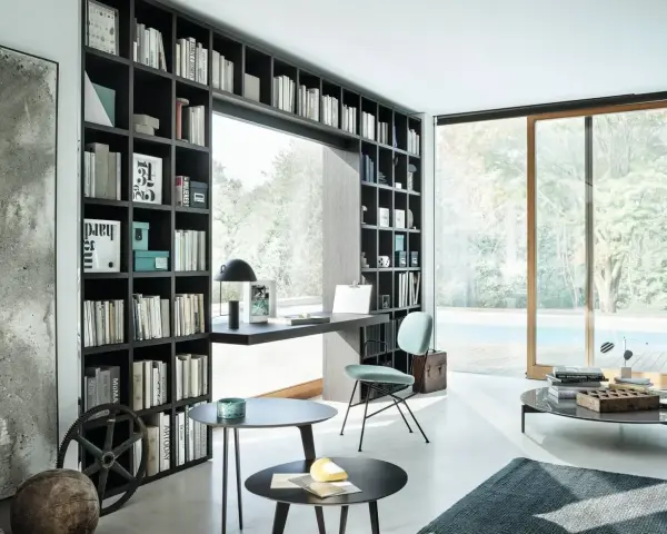 Libreria a muro con scrivania integrata, perfetta per idee stanza studio piccola. Sedia azzurra, tavolini neri e vista piscina.