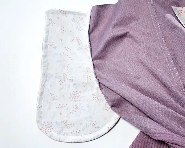 Détail d'un vêtement en cours de confection, montrant la doublure à motifs floraux des poches italiennes et le tissu extérieur violet.