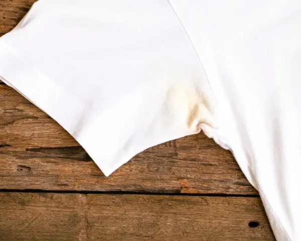 T-shirt blanc avec une tache jaune sous l'aisselle, sur un fond de bois rustique.