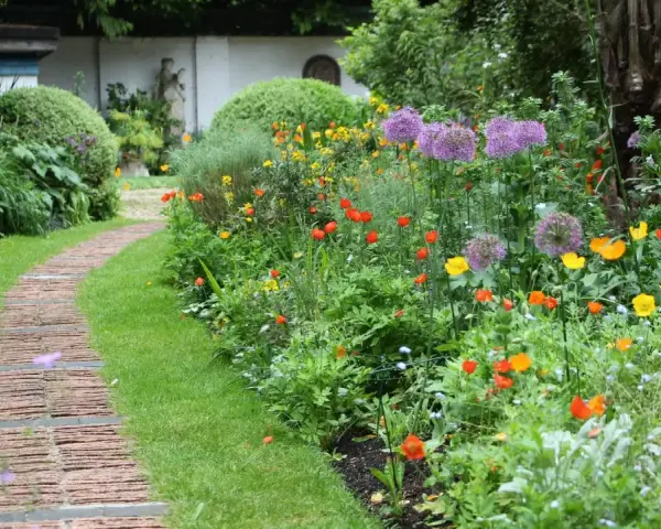 Ein geschwungener Weg aus Ziegelsteinen schlängelt sich durch einen üppigen bauerngarten mit leuchtenden Blumen und grünem Rasen.