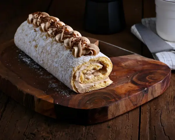 Un delicioso brazo de gitano cubierto de azúcar glas y decorado con crema de café y virutas de chocolate, listo para ser servido.