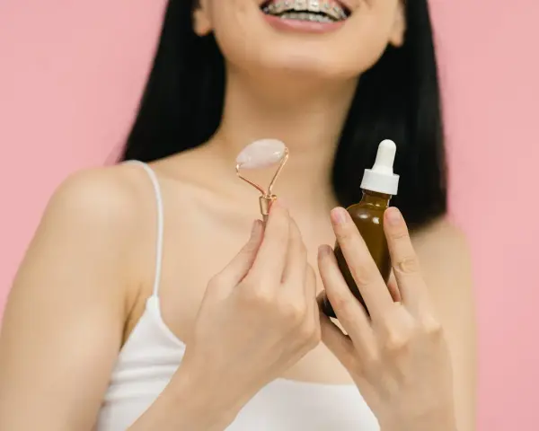 Uśmiechnięta kobieta z aparatem ortodontycznym trzyma jadeitowy roller i serum. Rozpoczyna wprowadzanie retinolu do swojej rutyny pielęgnacyjnej.