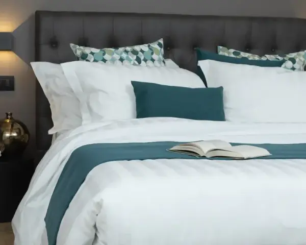 Letto con trapunta bianca a righe, cuscini coordinati e un libro aperto. Ecco come mettere la trapunta nel letto per un riposo perfetto.