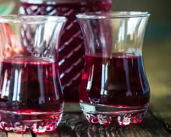 Dwa kieliszki wypełnione rubinową nalewką z czeremchy, obok butelka i kiść owoców.