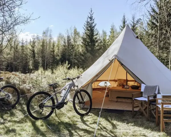 Två elcyklar står redo för äventyr vid ett stort tält på Bengts camping. Skogen bakom bjuder in till utforskning.