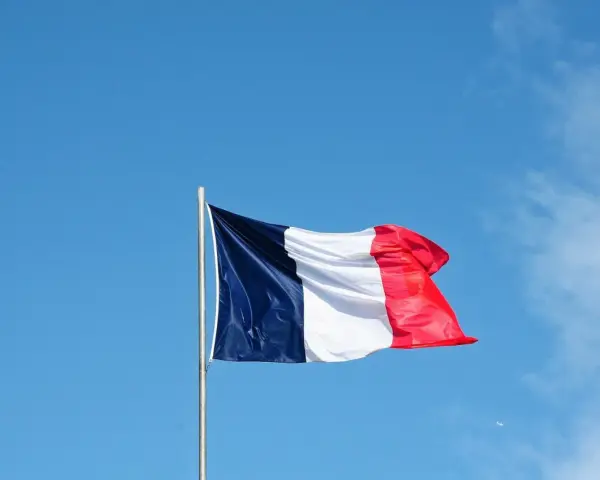 Die französische Flagge weht im Wind vor blauem Himmel. Ein Symbol für ein spannendes Auslandsjahr in Frankreich.