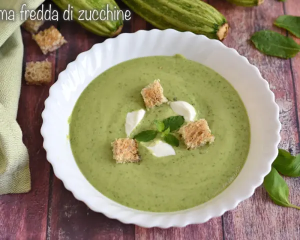 Crema fredda di zucchine servita in una ciotola bianca, guarnita con crostini, panna e menta. Fresca e invitante.