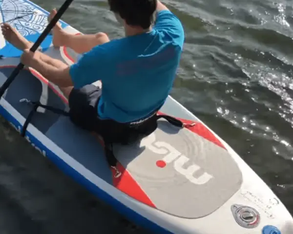 Mann sitzt auf SUP-Board, paddelt und befestigt den Sitz.