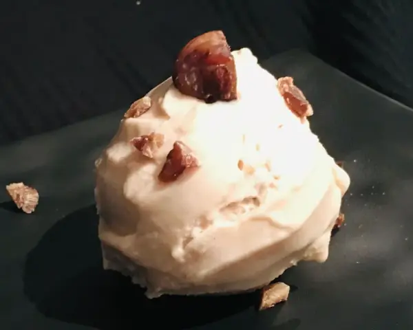 Cremiges Maronen Eis, garniert mit kleinen Maronenstückchen, auf einem dunklen Teller. Ein Genuss für kalte Tage.