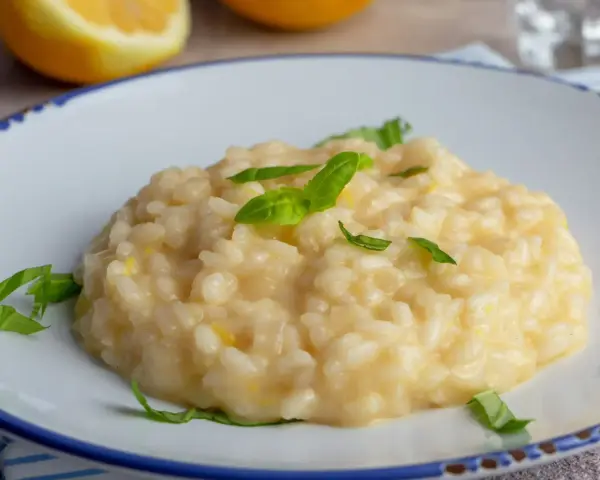 Kremowe, letnie risotto z cytryną i bazylią, podane na białym talerzu z niebieskim rantem.