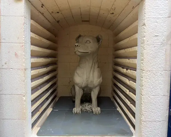 En hundskulptur i blålera keramik väntar på att brännas i en ugn.