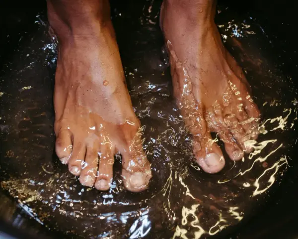 A close-up of feet soaking in a dark basin, likely a relaxing foot bath with epsom salt for feet.