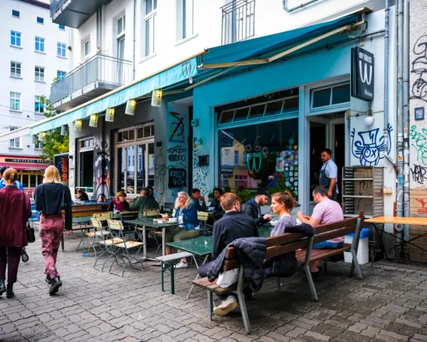 Menschen sitzen an Tischen vor einem **Prenzlauer Berg Restaurant** mit türkisfarbener Markise und Graffiti.