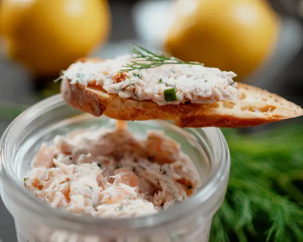 Un toast garni de rillettes de saumon, décoré d'aneth, avec un pot de rillettes en arrière-plan.