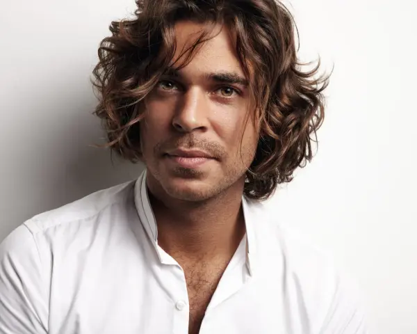 Hombre con cabello castaño ondulado, un ejemplo de cortes de pelo hombre medio largo, viste camisa blanca.