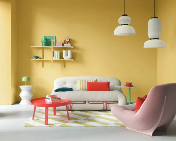 Ein Wohnzimmer mit gelben Wänden und einer auffälligen farb kombination aus Rot, Rosa und Weiß. Ein flauschiges Sofa und ein Sessel laden zum Entspannen ein.
