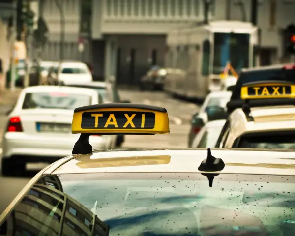 Ein Taxi mit leuchtendem "TAXI"-Schild auf dem Dach, bereit für Fahrten, auch im nachttarif. Regentropfen auf der Windschutzscheibe.