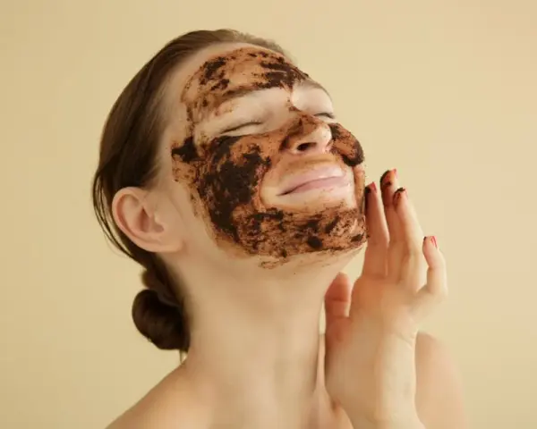 Mujer disfrutando de una mascarilla de café para la cara, con los ojos cerrados y una sonrisa.