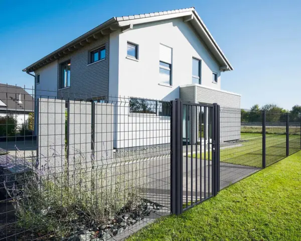 Une clôture privative en limite de propriété délimite un jardin moderne avec une maison blanche et un portillon.
