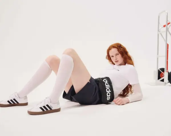 Rudowłosa modelka w białej koszulce i czarnych spodenkach z logo Adidas leży na podłodze. Czy Adidas ma zawyżoną rozmiarówkę?