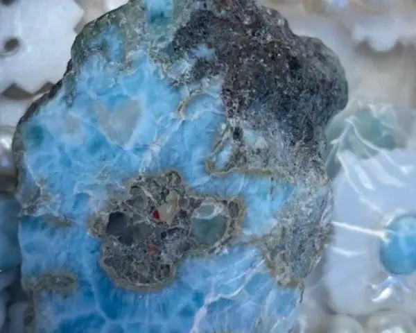 Surowy larimar, kamień o niebiesko-białych żyłkach, otoczony perłami i ozdobami. Jego magiczne właściwości uspokajają i przynoszą harmonię.