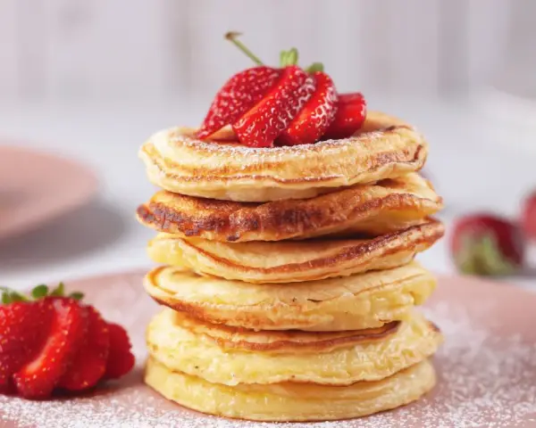 Pancakes dorati, perfetti per una ricetta pancake veloce senza lievito, guarniti con fragole fresche e zucchero a velo.