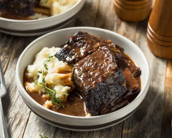 Un succulento brasato di manzo servito con purè di patate e guarnito con timo fresco.